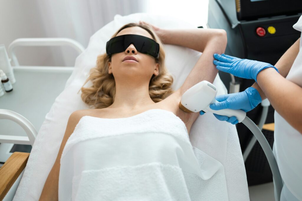 Beautician removing hair of young woman's armpit